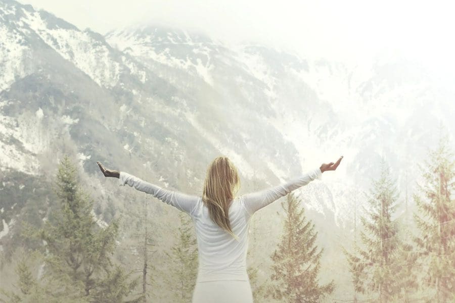 A woman standing in front of some trees with her arms outstretched.