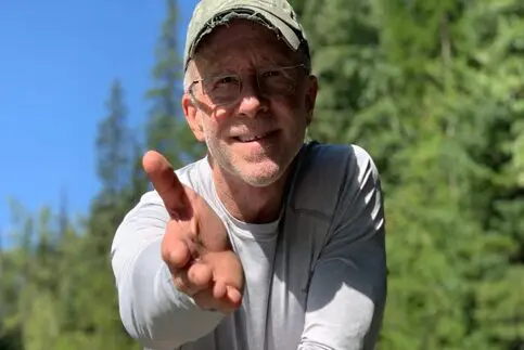 A man in white shirt and hat holding his hand up.