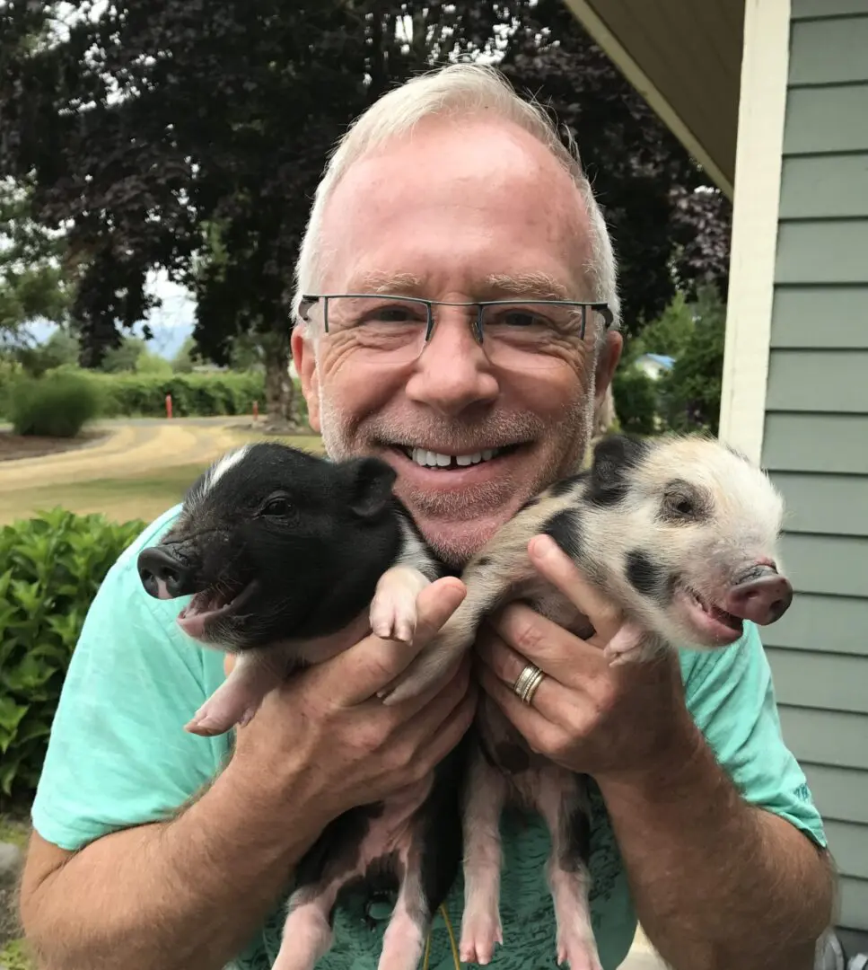 A man holding two baby pigs in his hands.
